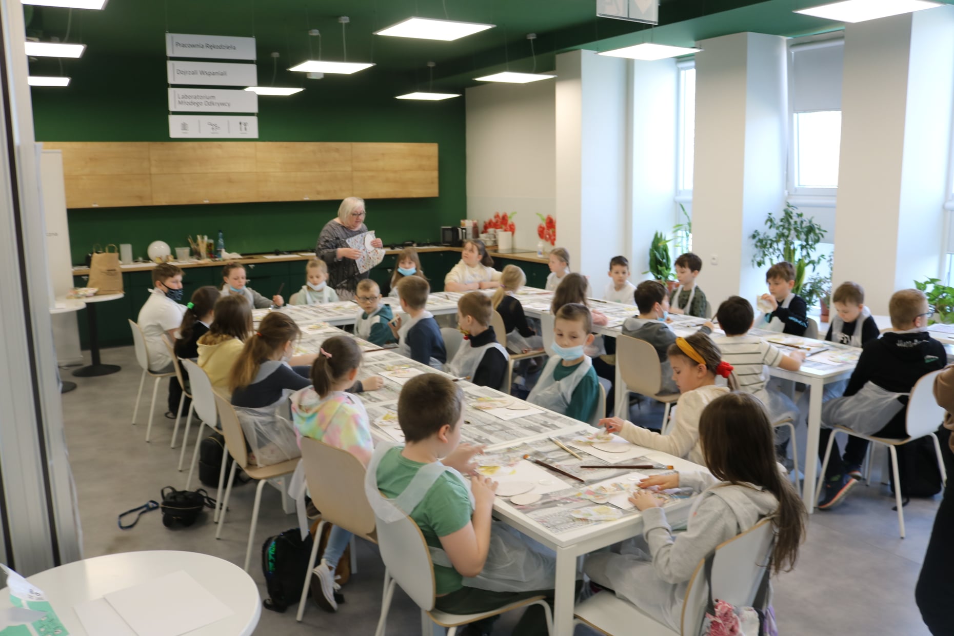 Dzieci siedzące przy stole i wykonujące prace ręczne podczas lekcji bibliotecznej w pracowni rękodzieła